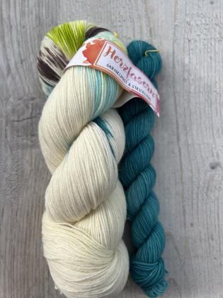 „Herzfasern No. 20 – Soktober-Set Wiesentanz: ein 100 g Strang in Creme mit Sprenkeln in Limegrün, Smaragd und Braun, kombiniert mit einem 20 g Mini in kräftigem Smaragd. Handgefärbte deutsche Sockenwolle (75 % Schurwolle, 25 % Polyamid, 420 m/100 g).“