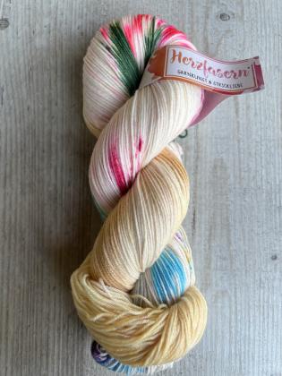Ein Strang Herzfasern No. 27 in der Färbung ‚Kugelzauber‘. Heller Grundton mit Farbakzenten in Pink, Grün, Türkis und Gold. Der Strang liegt auf hellem Untergrund.