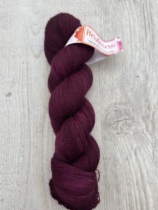 Ein Strang handgefärbter Wolle in einem sehr dunklen, bordeauxroten Ton liegt auf hellem Holz. Der Strang ist gedreht, die feine Melierung der Faser ist gut erkennbar. Die Herzfasern-Banderole ist teilweise sichtbar.