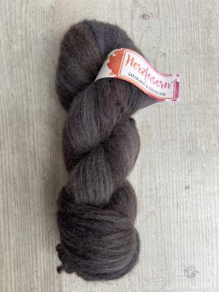 Das Foto zeigt einen flauschigen Strang Herzfasern No. 42 in einem tiefen, melierten Dunkelbraun. Die Oberfläche ist weich und leicht haarig. Der Strang liegt auf heller Holzoberfläche – oben sichtbar das Herzfasern-Etikett.