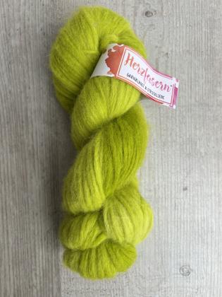 Ein locker gedrehter Strang Herzfasern No. 42 in einem leuchtenden, frischen Grünton. Das Garn wirkt weich, flauschig und leicht. Der Strang liegt auf einer hellen Holzoberfläche, darüber ein Herzfasern-Etikett.