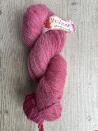 Das Foto zeigt einen flauschigen, locker gedrehten Strang in einem warmen Beerenton. Die Farbe wirkt samtig und leicht meliert. Der Strang liegt auf einer hellen Holzoberfläche, oben ist ein Herzfasern-Etikett sichtbar.