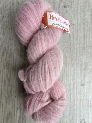 Ein locker gedrehter, flauschiger Strang der Herzfasern No. 42 in einem sehr zarten Roséton. Die Farbe ist pudrig, weich und gleichmäßig. Der Strang liegt auf einer hellen Holzoberfläche. Oben befindet sich ein Herzfasern-Etikett.