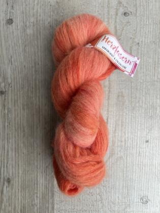 Das Bild zeigt einen flauschigen Strang Herzfasern No. 42 in einem warmen, koralligen Orangeton mit leichter Melierung. Der Strang liegt auf heller Holzoberfläche, oben ist ein Herzfasern-Etikett sichtbar.