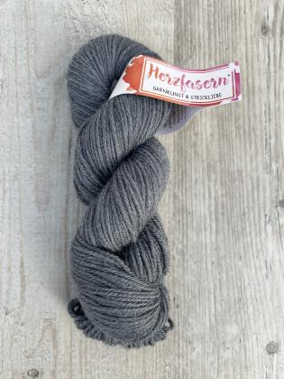 Handgefärbter Wollstrang Herzfasern No. 46 aus Alpaka und Bio-Schurwolle in ruhigem Anthrazit, einem mittleren Dunkelgrau mit matter Oberfläche und leicht sichtbarem Alpaka-Flaum, fotografiert auf hellem Holzuntergrund.