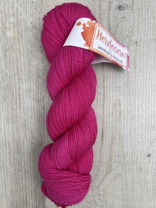 Ein Strang handgefärbter Wolle in intensivem, kräftigem Pink. Der Strang liegt auf hellem Holz, das Garn glänzt leicht seidig und wirkt weich und glatt. Das Herzfasern-Etikett ist sichtbar.