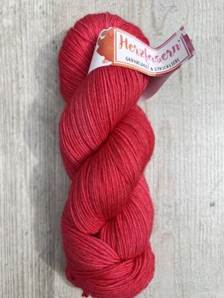 Ein Strang handgefärbte Wolle in kräftigem, leuchtendem Rot. Garnbasis Herzfasern No. 92 (65 % Schurwolle, 22 % Kaschmir, 13 % Seide), fotografiert auf hellem Holzuntergrund.