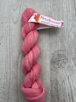 Ein roséfarbener, flauschiger Lace-Strang aus Cashmere und Seide (Herzfasern No. 93) liegt auf hellem Holz. Der Strang trägt eine Herzfasern-Banderole.“