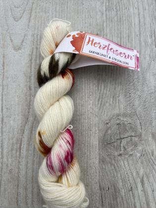 Ein handgefärbter Strang Herzfasern No. 94 – Cashmere Cloud in der Farbe Herbstrose. Cremiger Grundton mit Akzenten in Rosé, Beere, Gold und Moosgrün. Fotografiert auf hellem Holz mit Herzfasern-Banderole.