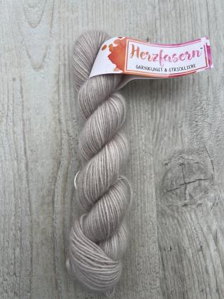 Ein handgefärbter Strang Herzfasern No. 94 – Cashmere Cloud in der Farbe Perlmutt. Zarter Schimmer zwischen Creme, Rosé und Silber, edel und ruhig. Fotografiert auf hellem Holz mit Herzfasern-Banderole.