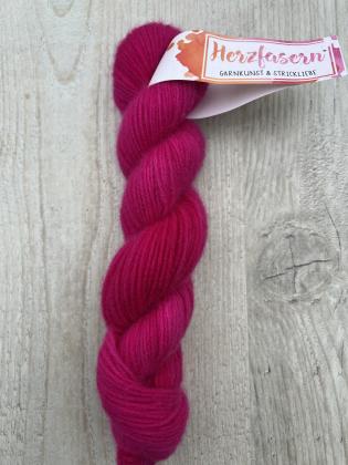 Ein handgefärbter Strang Herzfasern No. 94 – Cashmere Cloud in der Farbe Herzfasern-Pink. Intensives, leuchtendes Pink mit feinem Schimmer, fotografiert auf hellem Holz mit Herzfasern-Banderole.