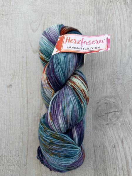 Mehrere handgefärbte Garnstränge der Marke Herzfasern liegen nebeneinander. Die Färbung „Umbruch“ zeigt bewegte, kontrastreiche Farbtöne mit sichtbaren Übergängen. Die Farbwirkung ist lebendig und dynamisch.