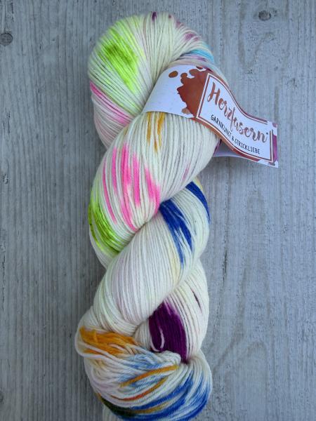 Handgefärbter Wollstrang in hellem Naturton mit unregelmäßigen Farbflächen in Pink, Grün, Violett, Gelb und Blau. Die Farben sind locker verteilt und verlaufen weich ineinander, wodurch jeder Strang unterschiedlich wirkt.