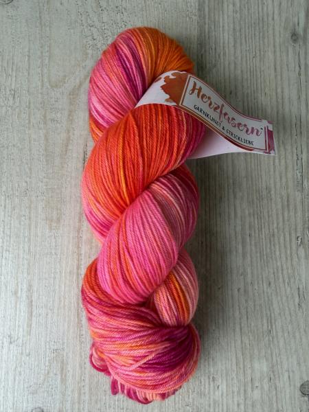 Handgefärbter Wollstrang „Neonherz“ auf Herzfasern No. 11 in leuchtenden Pink-, Korall- und Orangetönen mit weichen Farbverläufen auf hellem Holzuntergrund.
