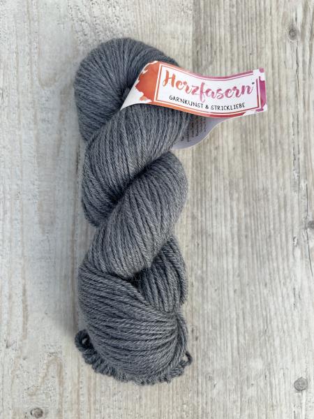 Handgefärbter Wollstrang Herzfasern No. 46 aus Alpaka und Bio-Schurwolle in ruhigem Anthrazit, einem mittleren Dunkelgrau mit matter Oberfläche und leicht sichtbarem Alpaka-Flaum, fotografiert auf hellem Holzuntergrund.