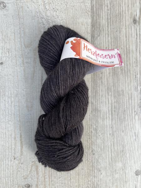 Handgefärbter Wollstrang Herzfasern No. 46 aus Alpaka und Bio-Schurwolle in tiefem, warmem Dunkelbraun („Schokoschatten“), mit matter Oberfläche und sichtbarem Alpaka-Flaum, fotografiert auf hellem Holzuntergrund.