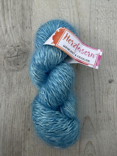 Handgefärbter Wollstrang in Türkis- und Aquatönen auf Herzfasern No 50 (Seide-Mohair-Garn), liegend auf hellem Holzuntergrund fotografiert, mit Herzfasern-Banderole.