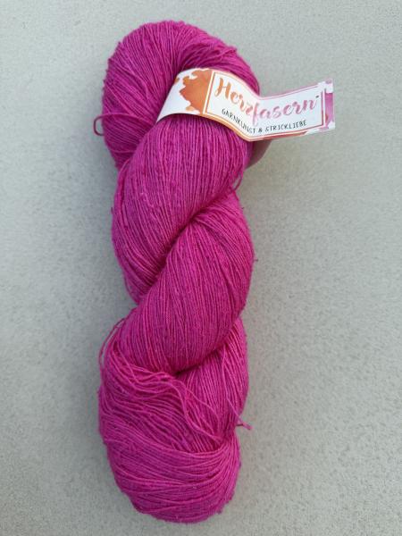 Ein handgefärbter Strang Tussahseide in kräftigem Pink liegt auf hellem Untergrund. Die feine, leicht unregelmäßige Garnstruktur mit kleinen Noppen ist gut sichtbar. Eine Banderole mit der Aufschrift „Herzfasern“ ist am Strang befestigt.