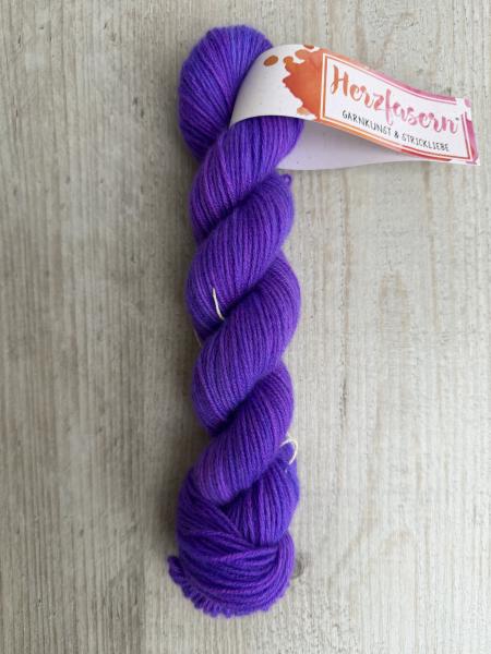 Handgefärbter Strang Herzfasern No. 94 Kaschmir-Cloud in kräftigem, sattem Lila auf hellem Holzhintergrund mit Herzfasern-Banderole.