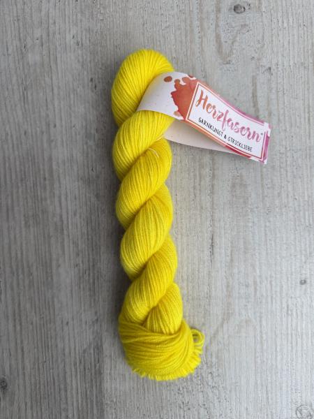 Handgefärbter Strang Herzfasern No. 94 Kaschmir-Cloud in kräftigem, leuchtendem Gelb auf hellem Holzhintergrund mit Herzfasern-Banderole.