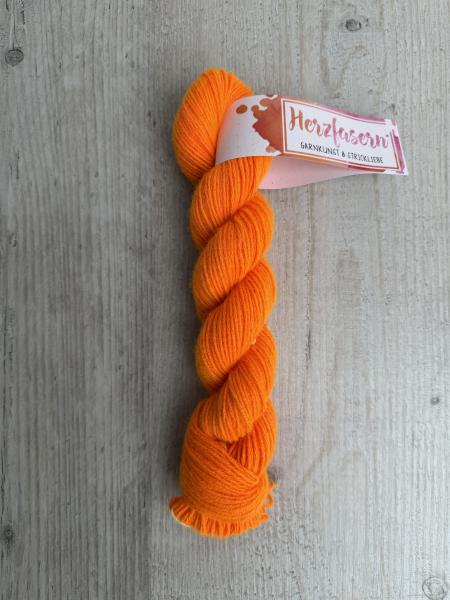 Handgefärbter Strang Herzfasern No. 94 Kaschmir-Cloud in kräftigem Neon-Orange auf hellem Holzhintergrund, mit Herzfasern-Banderole.