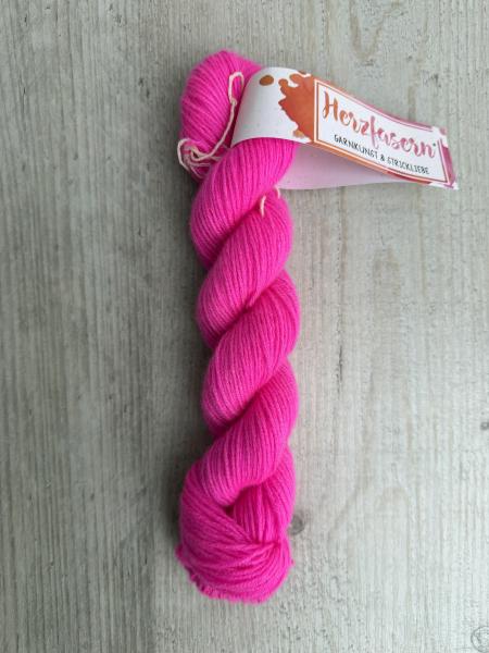 Strang aus 100 Prozent Kaschmir in leuchtendem Neon-Fuchsia mit Herzfasern-Banderole auf hellem Holzuntergrund.